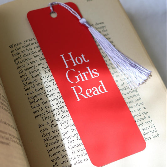 A red bookmark with the text 'HOT GIRLS READ' and a tassel, placed on an open book.